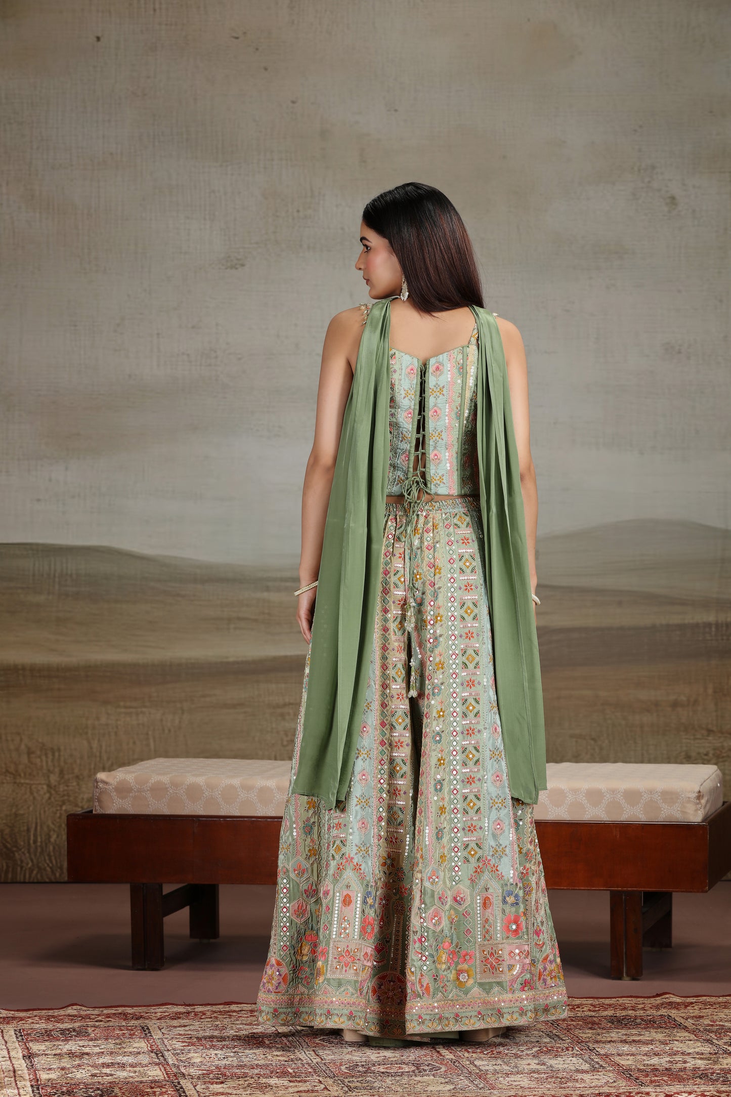Woman in a green and patterned outfit standing in a room with a neutral background
