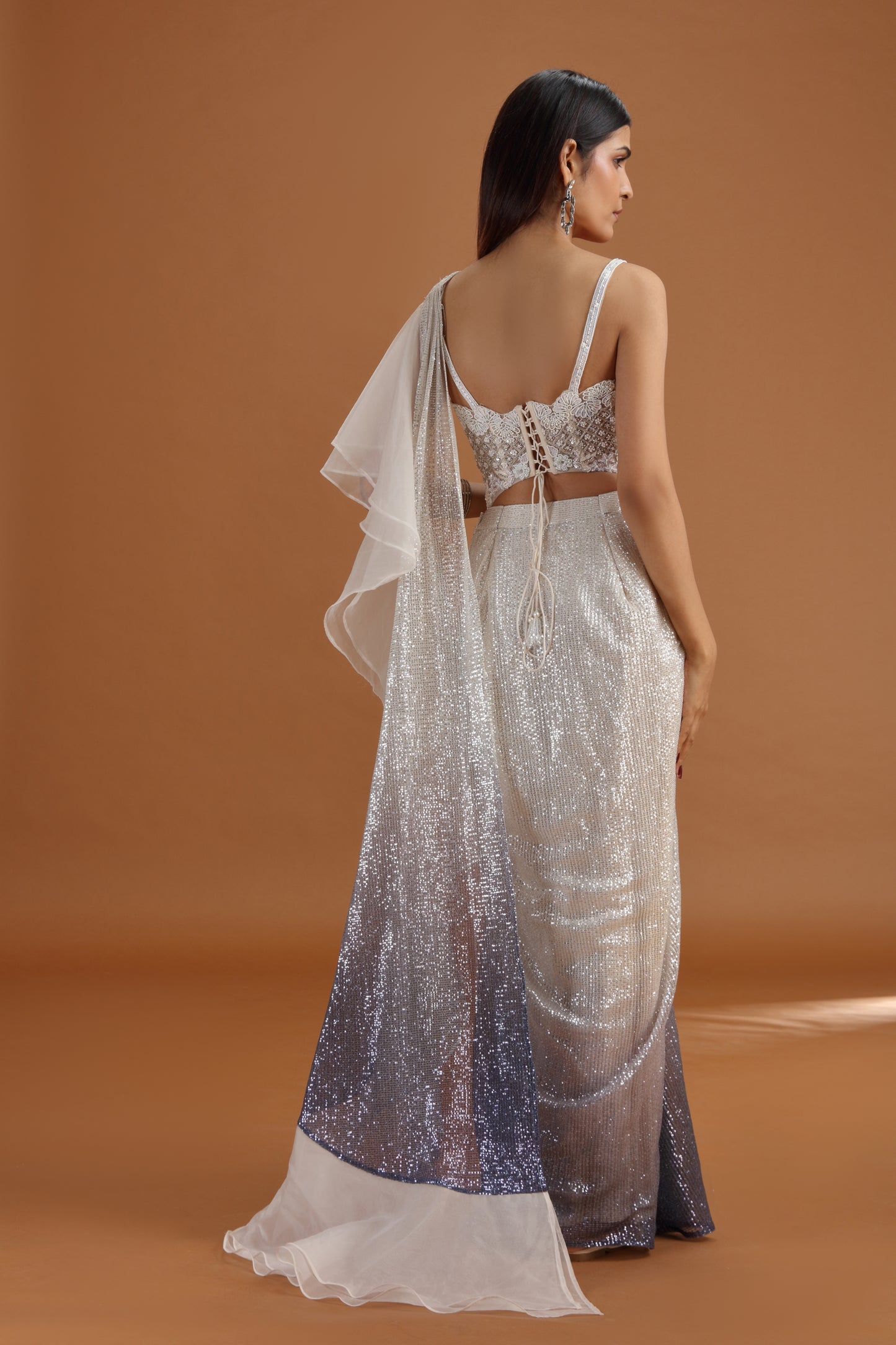 Woman wearing a off white silver saree with a plain background