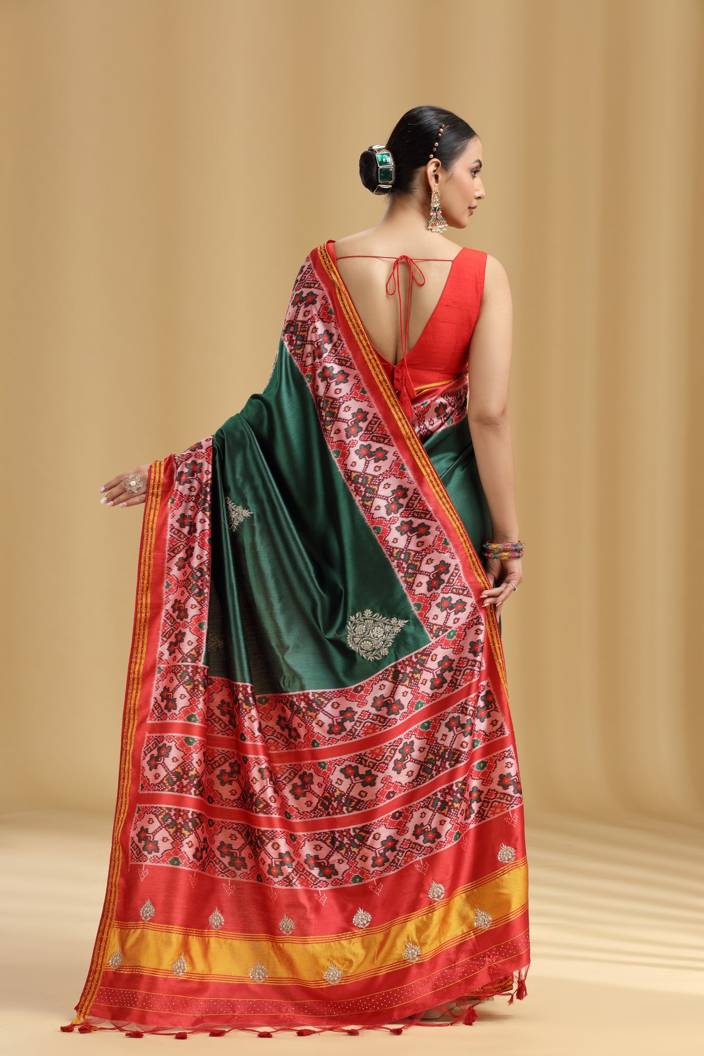 Woman wearing a green and red saree with a patterned border on a beige background