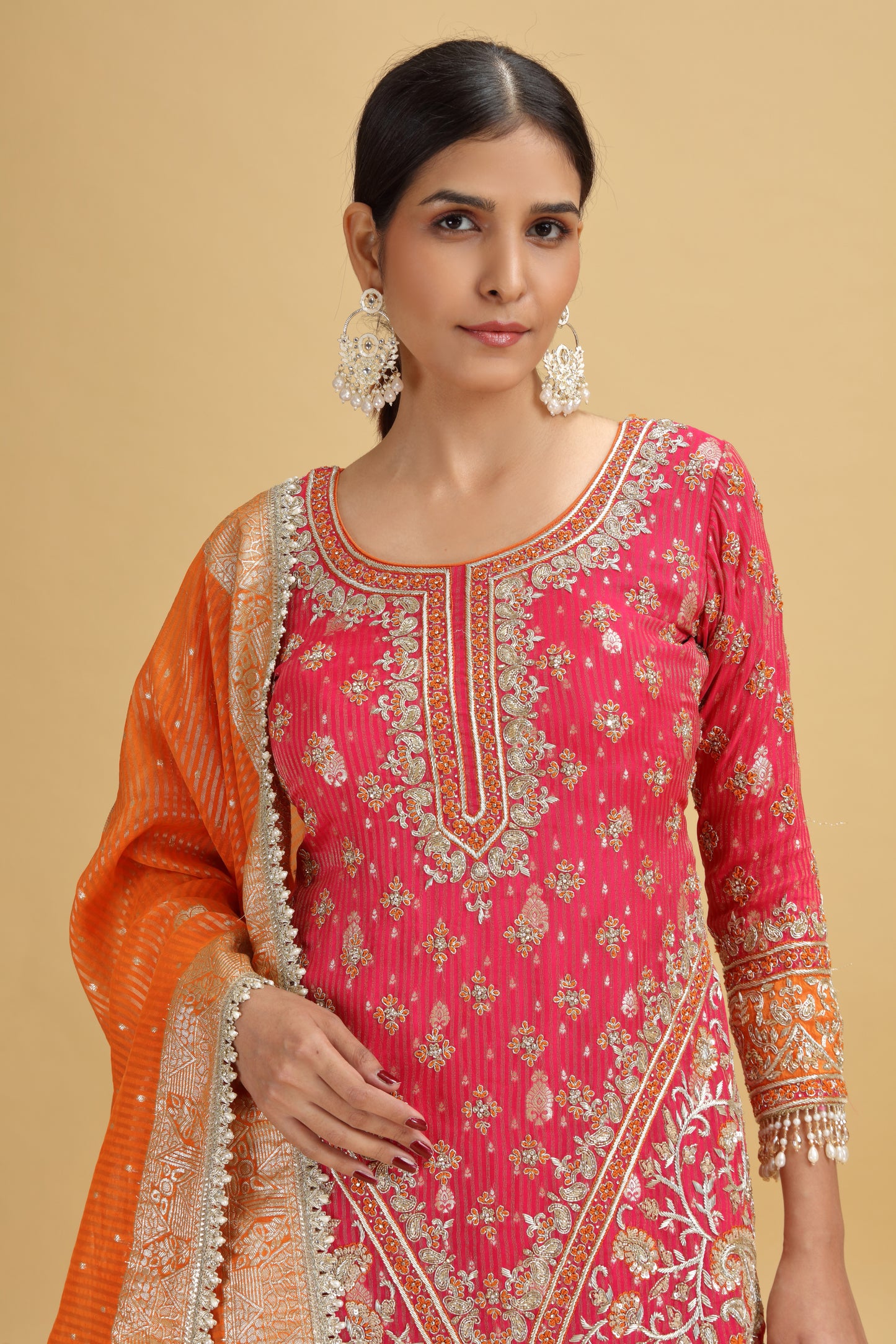 Woman wearing a pink and orange traditional salwar suit set with patterns on a beige background