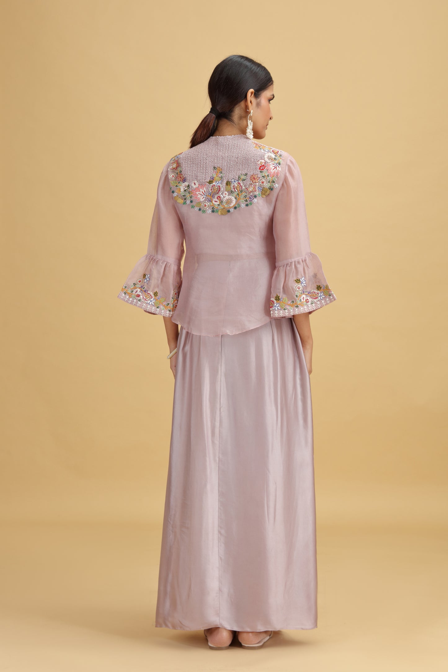 Woman wearing a light pink traditional outfit with floral embroidery on a beige background