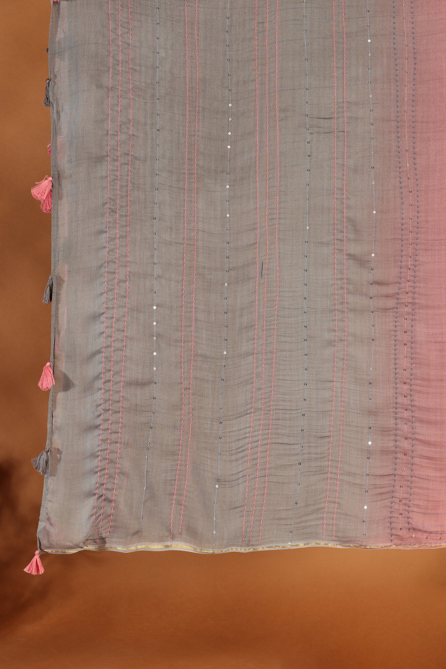 A close-up of a fabric with vertical pink lines and small sequins on a muted brown background