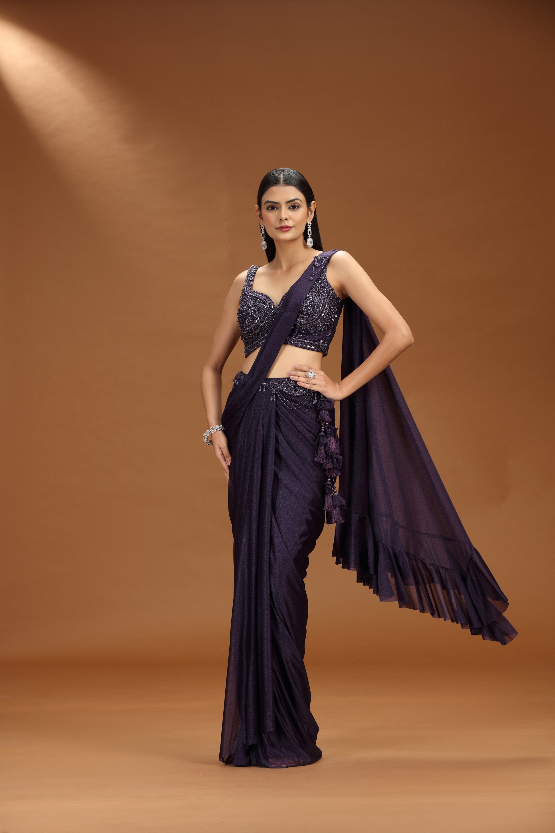 Woman wearing a dark purple saree with a matching blouse against a brown background