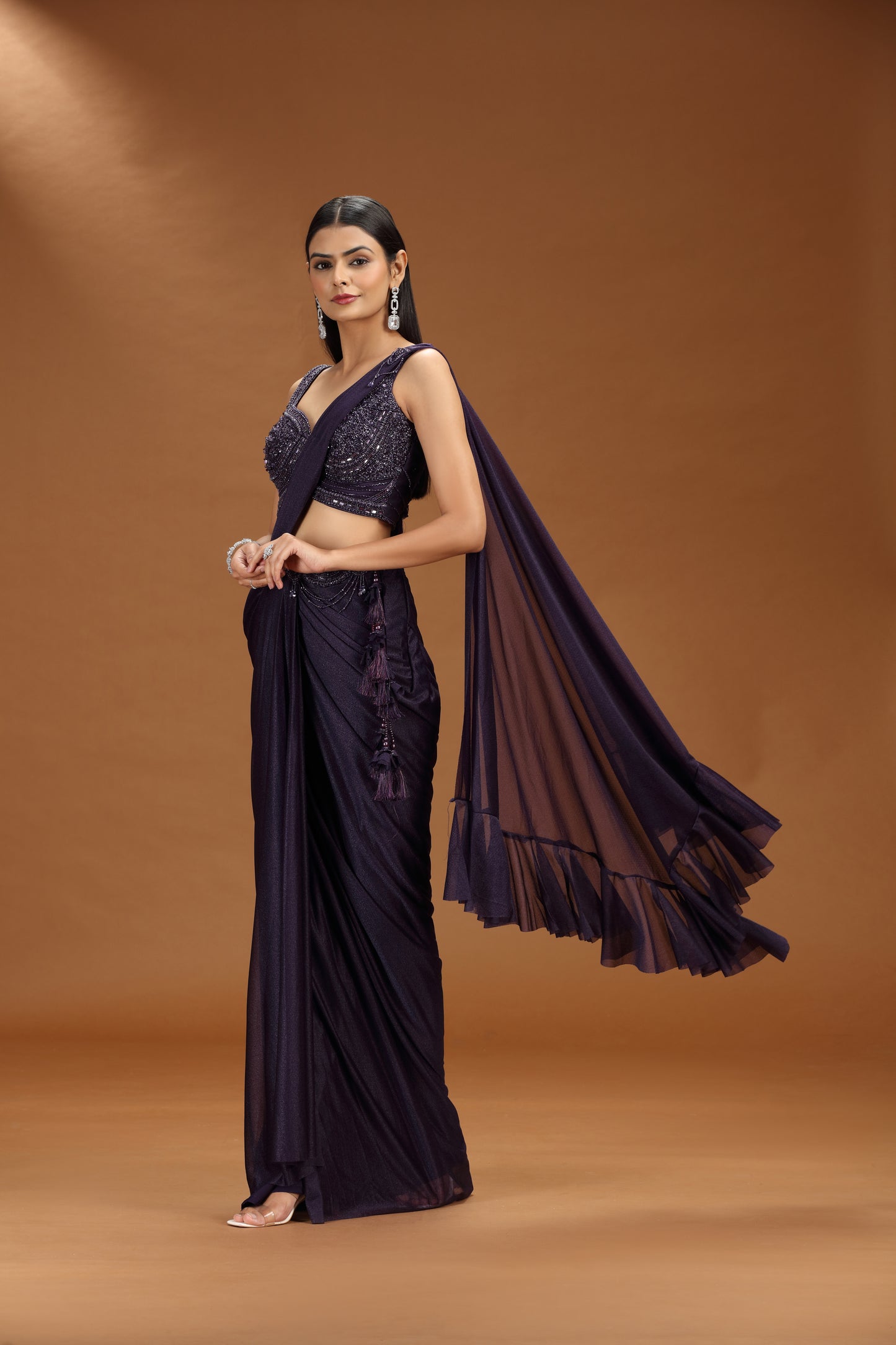 Woman in a purple saree with a matching blouse against a brown background