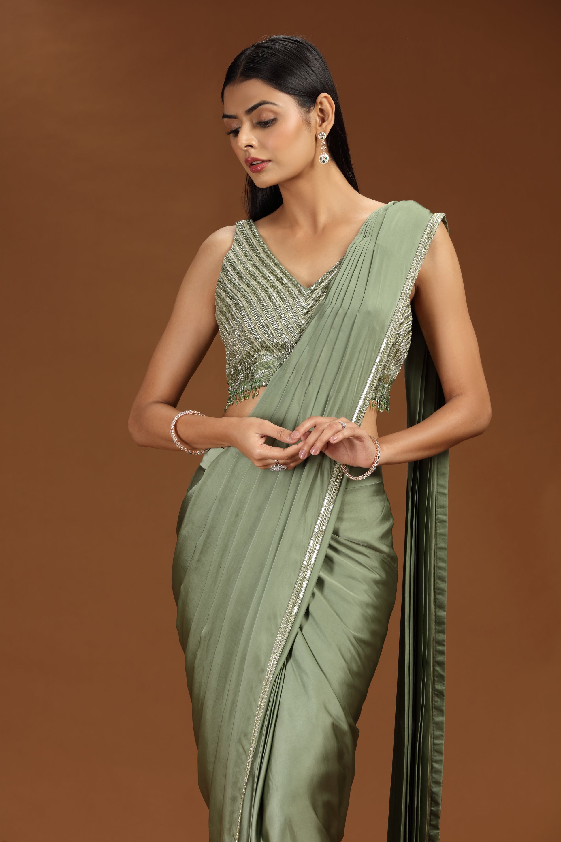Woman wearing a green saree with silver details against a brown background