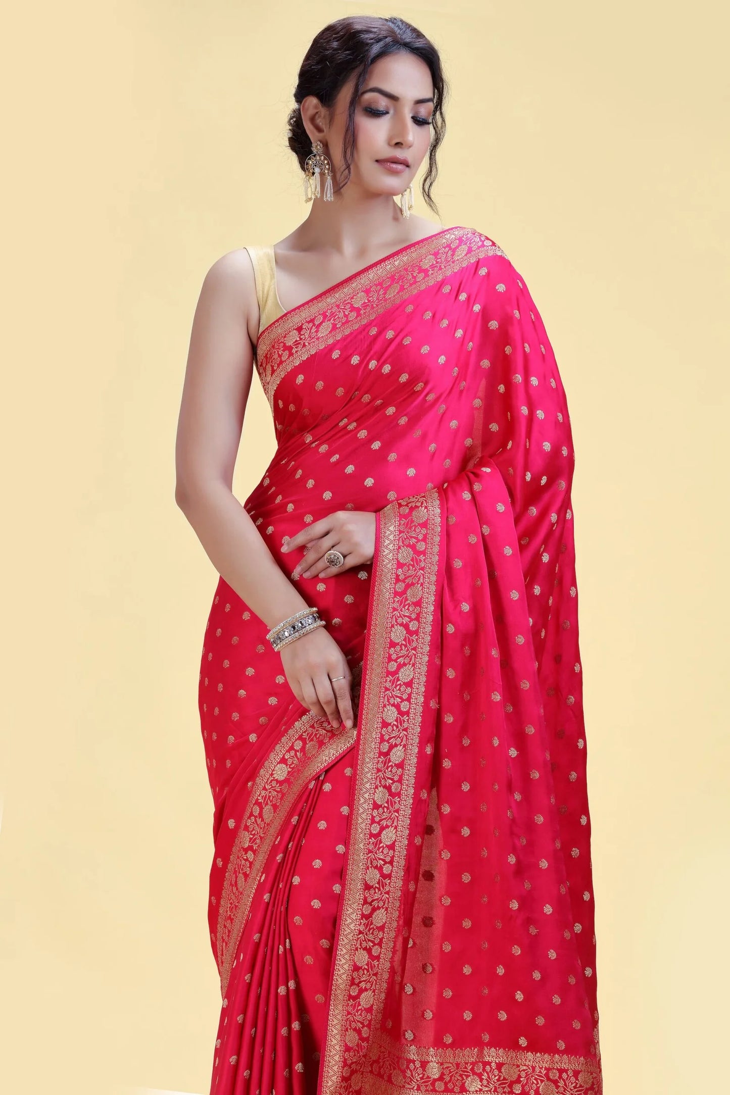 Woman in a vibrant red saree with gold detailing, wearing elegant silver jewelry, standing against a soft yellow background