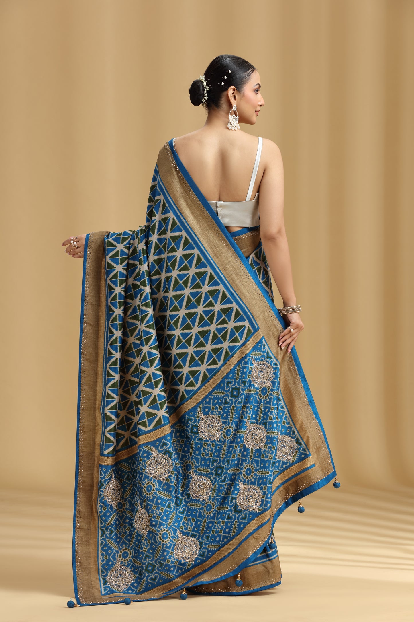 Woman wearing a blue and gold saree against a beige background