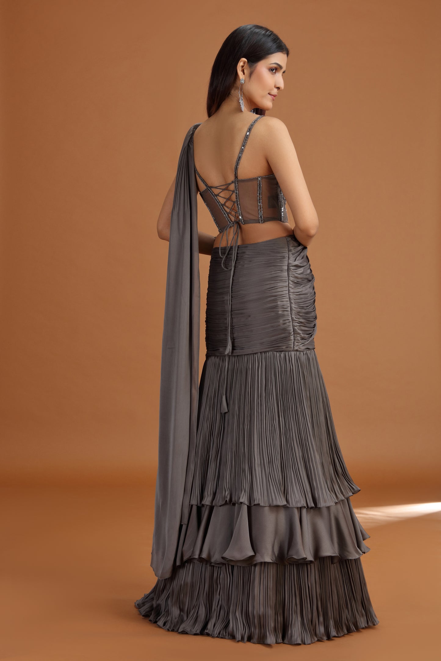 Woman wearing a dark grey lehenga set with a matching dupatta on an orange background