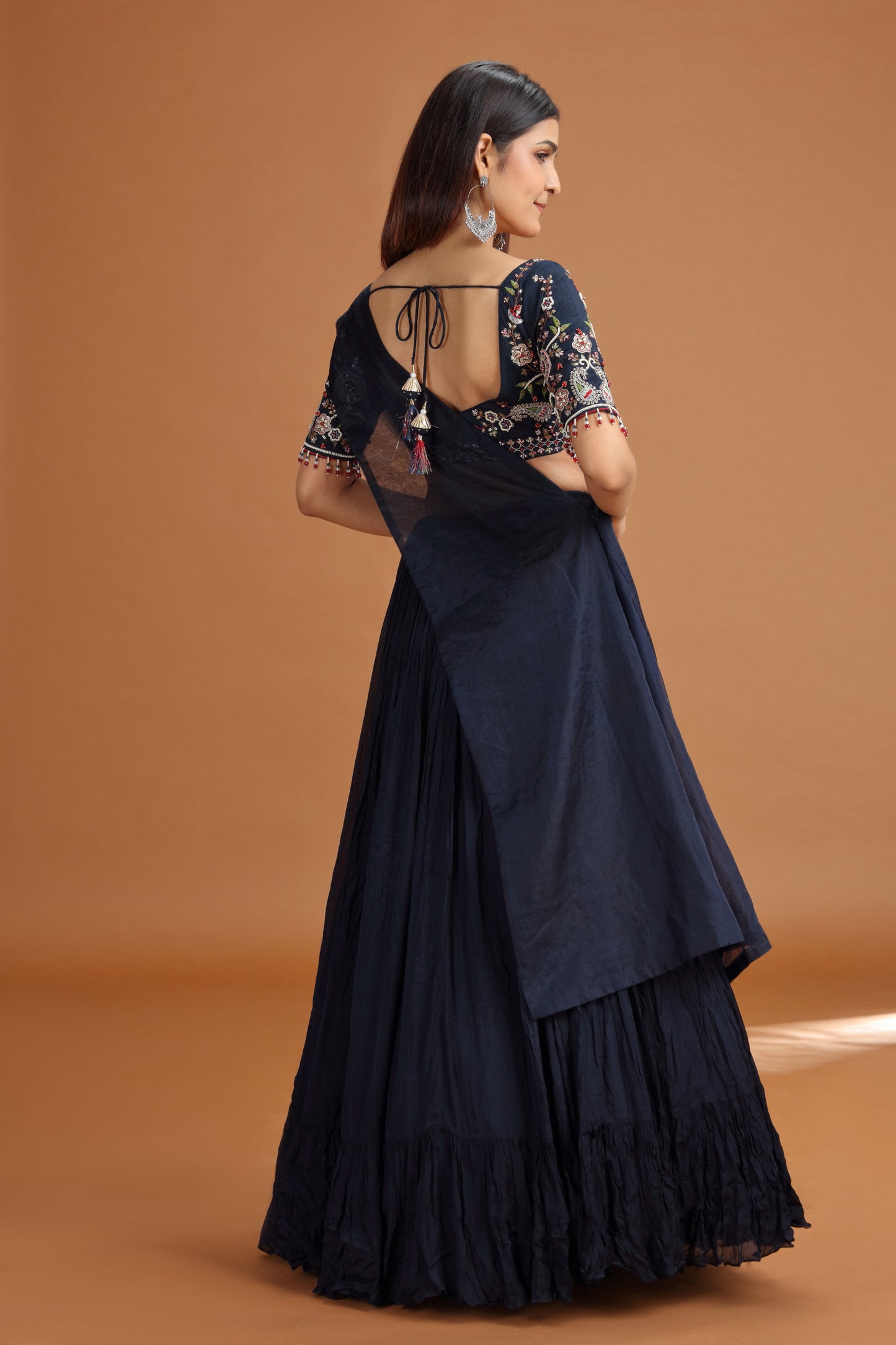 Woman wearing a dark blue lehenga with floral blouse against a brown background