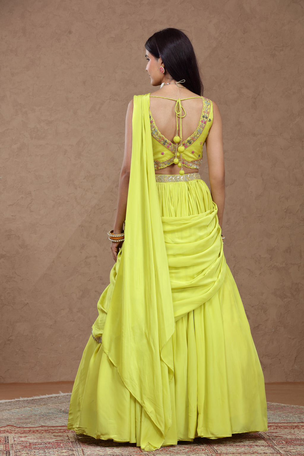Woman wearing a bright yellow traditional outfit with intricate detailing on a brown background