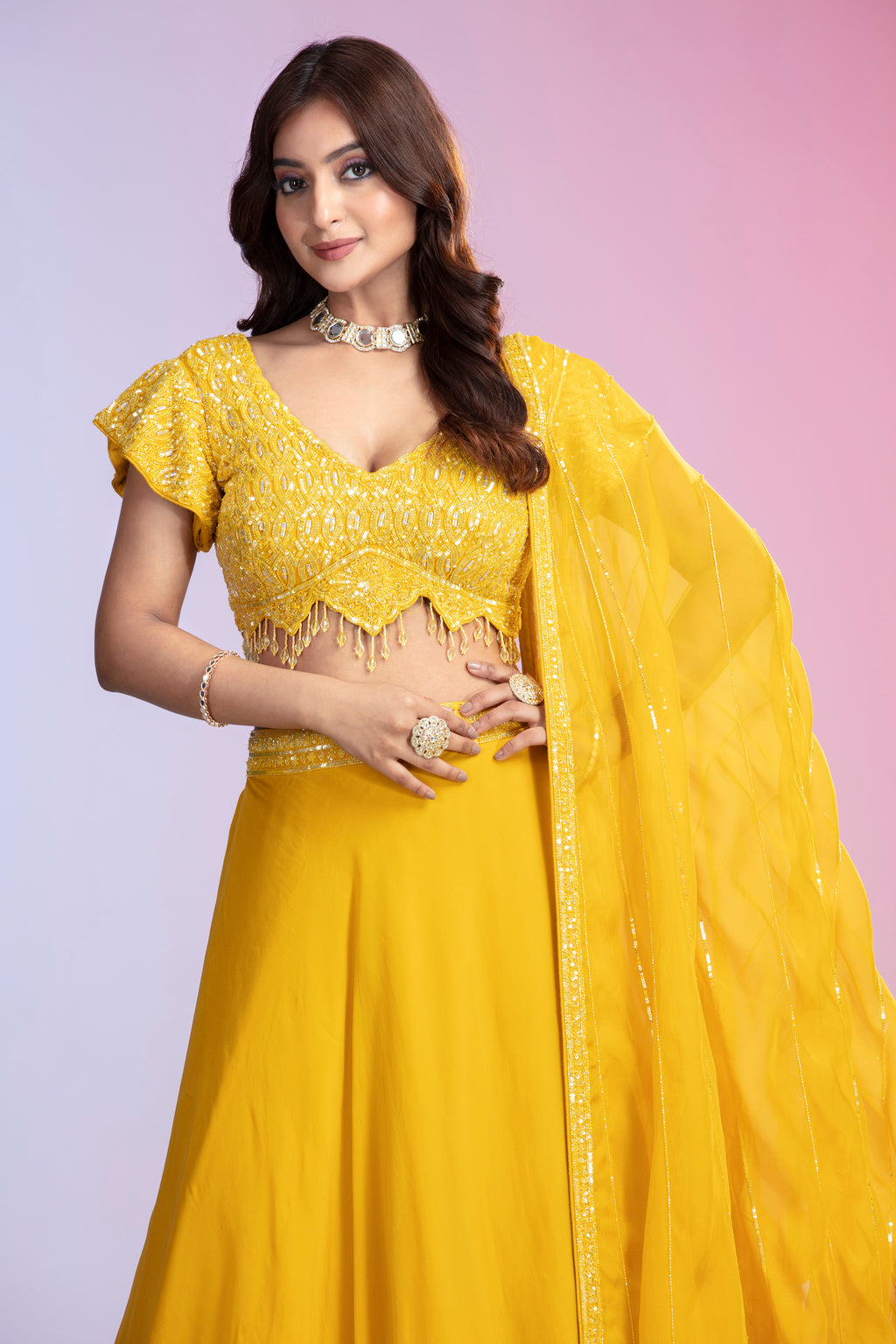 Woman in a vibrant yellow traditional outfit smiles against a pink background