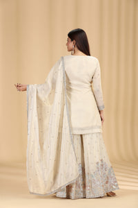 Woman wearing a cream traditional outfit with a matching dupatta on a beige background