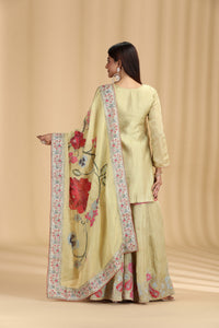 Woman wearing a light green traditional outfit with a floral dupatta on a beige background