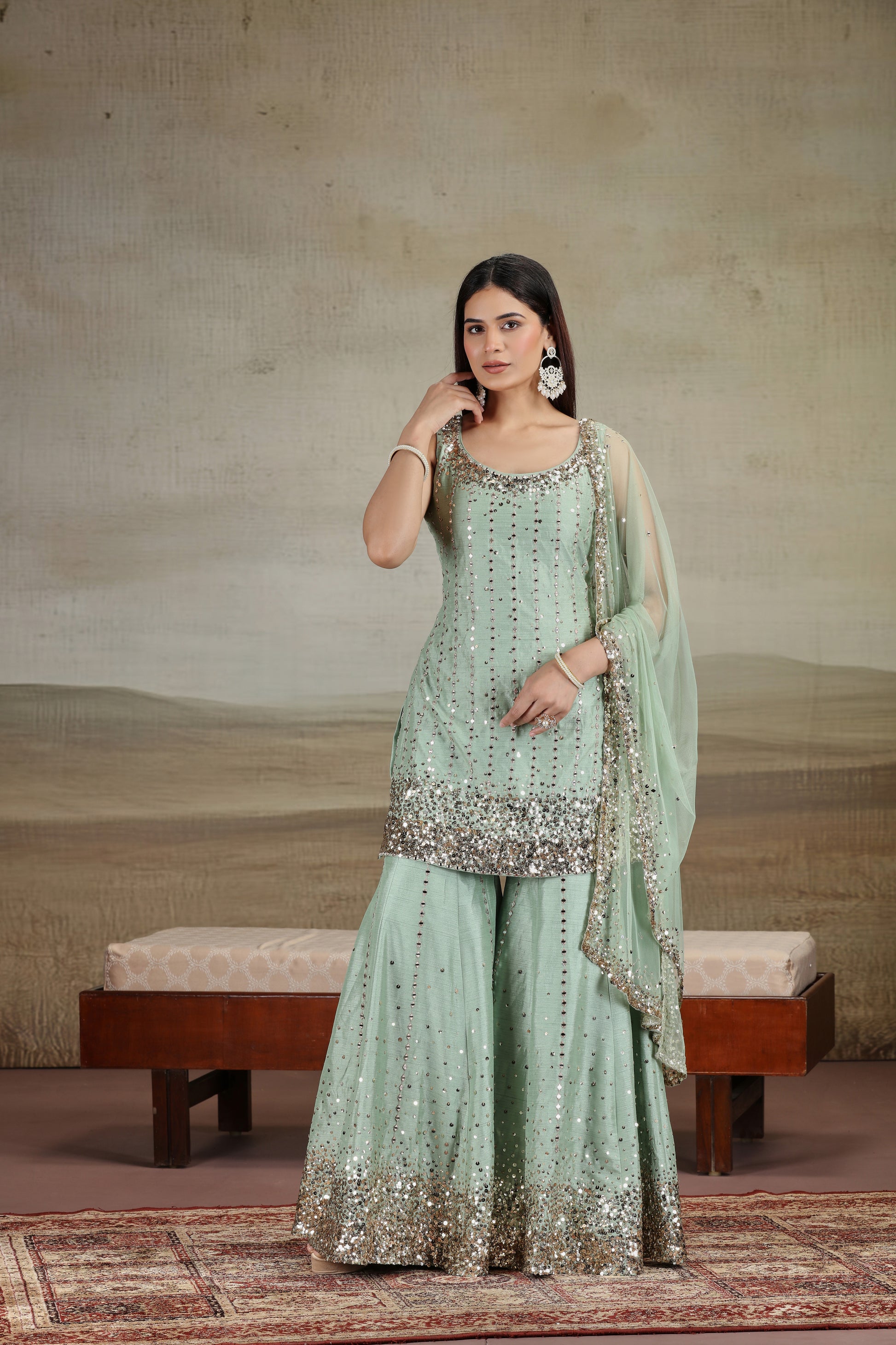 Woman in a light green traditional outfit with silver embroidery standing against a neutral background.