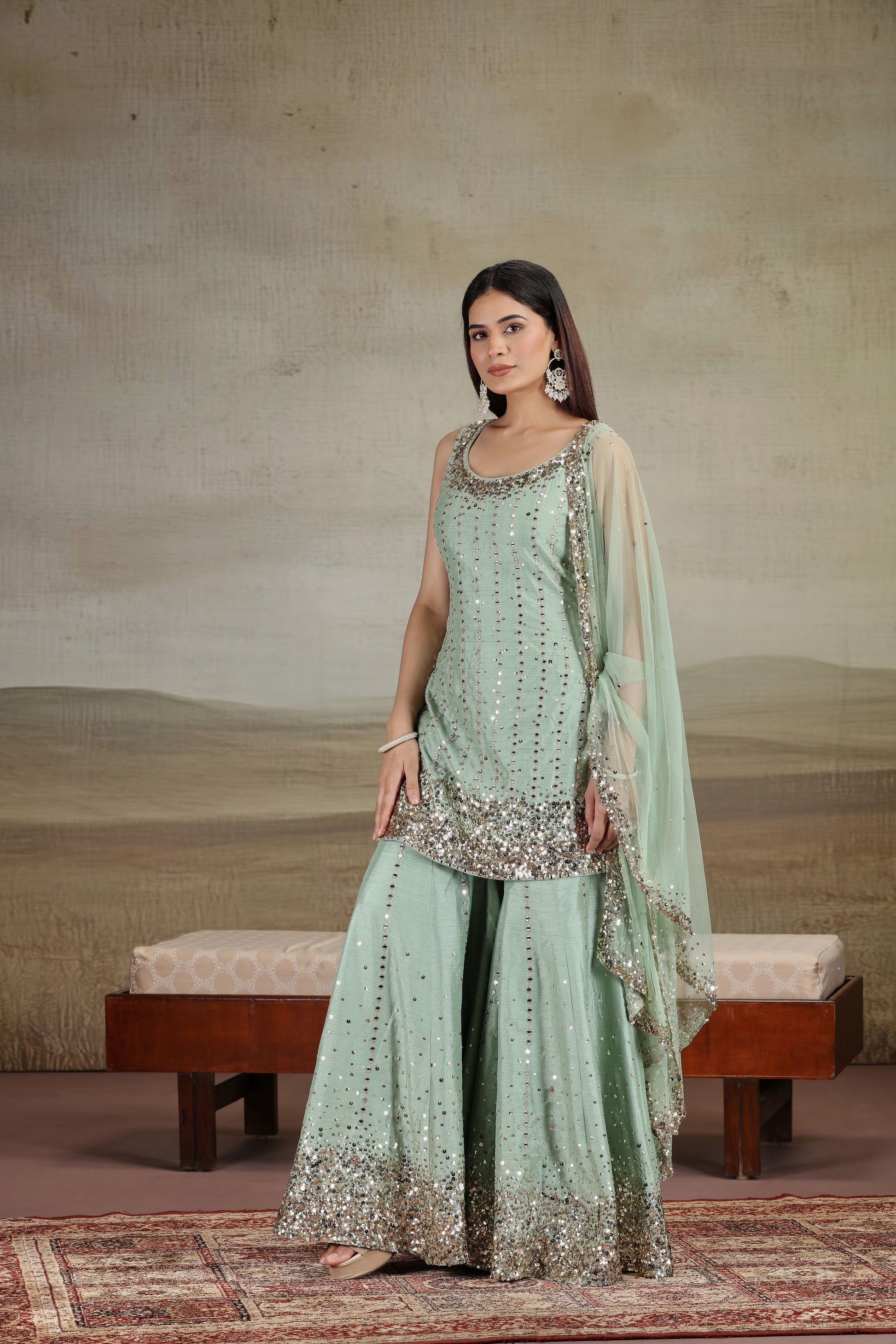 Woman in a light green traditional outfit with embroidery, standing against a neutral background.