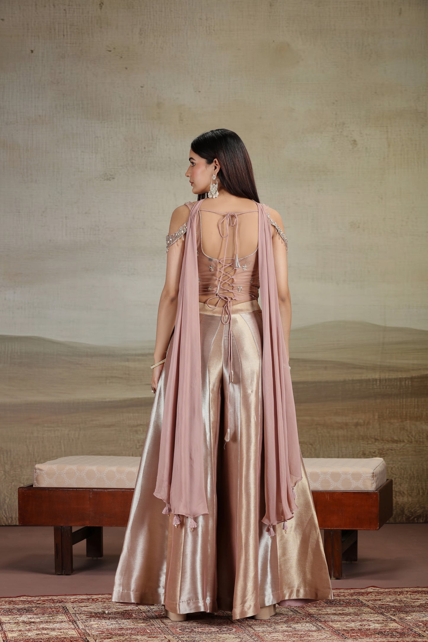 Woman in a elegant outfit with a beige and pink color scheme, standing against a neutral background.