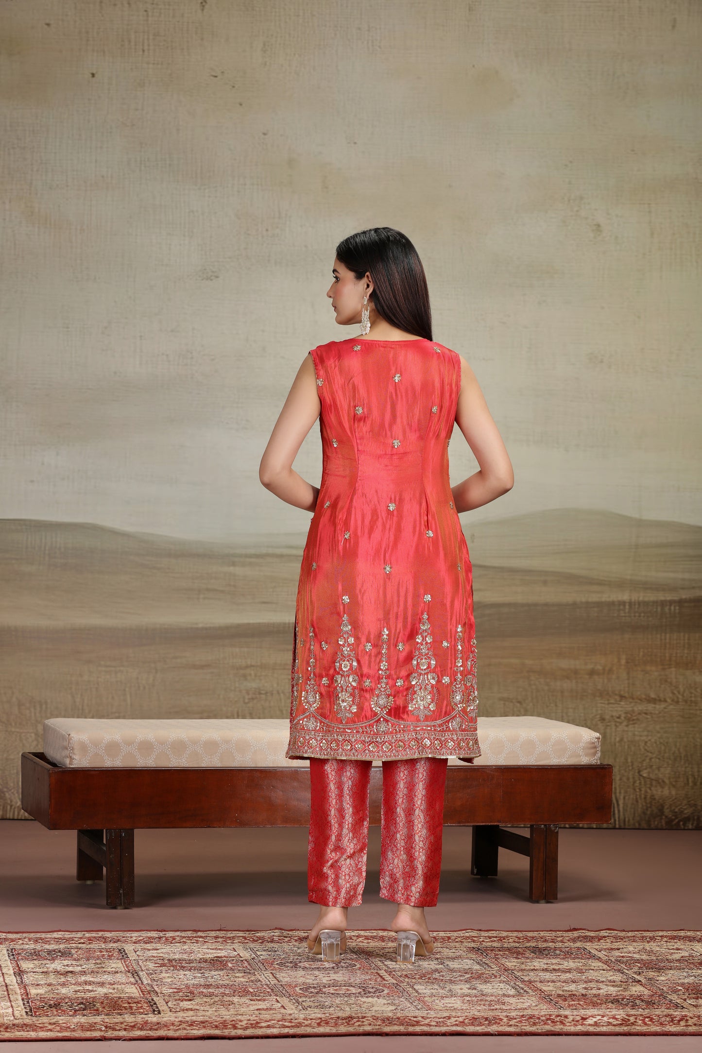 Woman in a red traditional outfit standing in front of a textured wall.