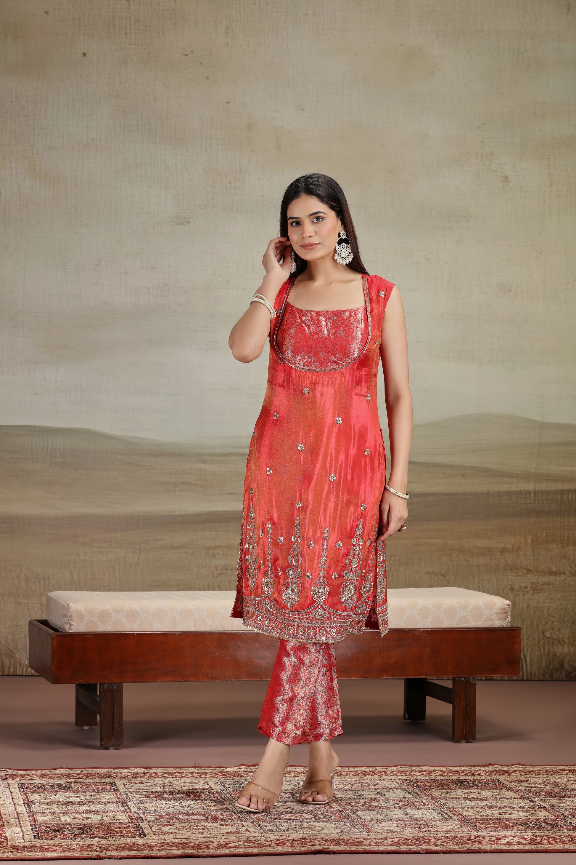 Woman in a red traditional outfit standing in front of a textured wall with a bench.
