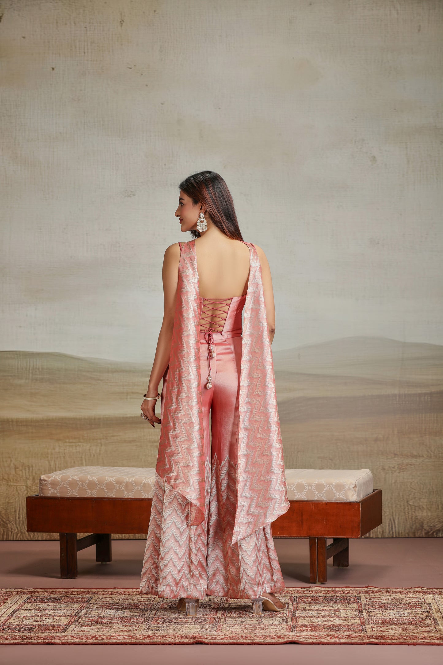 Woman in a peach banarasi silk suit outfit standing in a room with a textured wall and wooden bench.