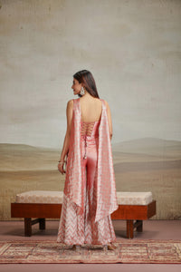 Woman in a peach banarasi silk suit outfit standing in a room with a textured wall and wooden bench.