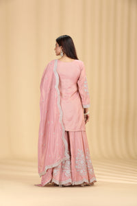 Woman wearing a pink traditional outfit with white embroidery on a beige background