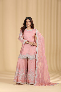 Woman wearing a pink traditional outfit with white embroidery against a beige background
