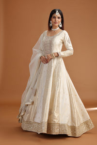 Woman wearing a Ivory Banarasi Silk Gown with gold details on a brown background