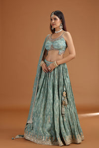 Woman wearing a traditional green and gold tissue lehenga with jewelry on a brown background