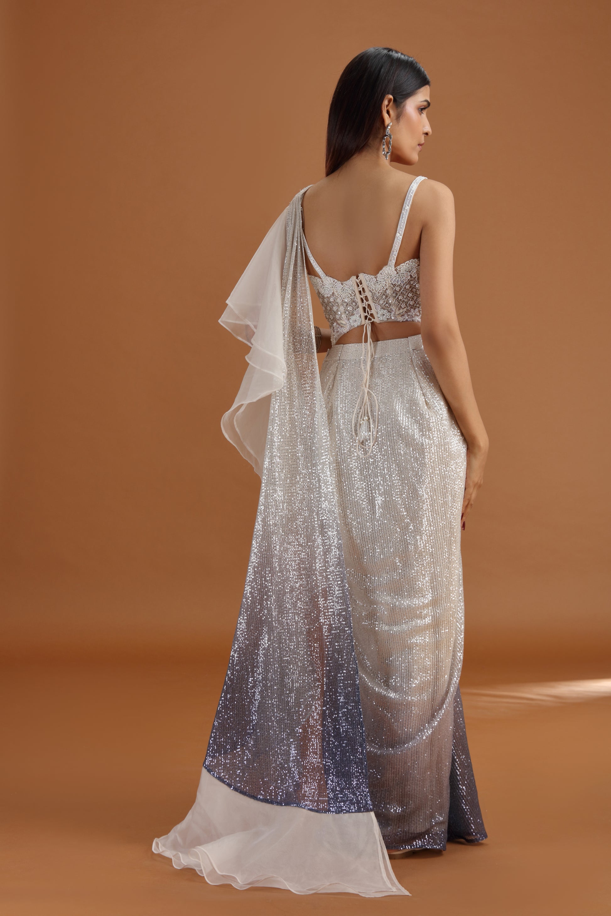 Woman wearing a off white silver saree with a plain background