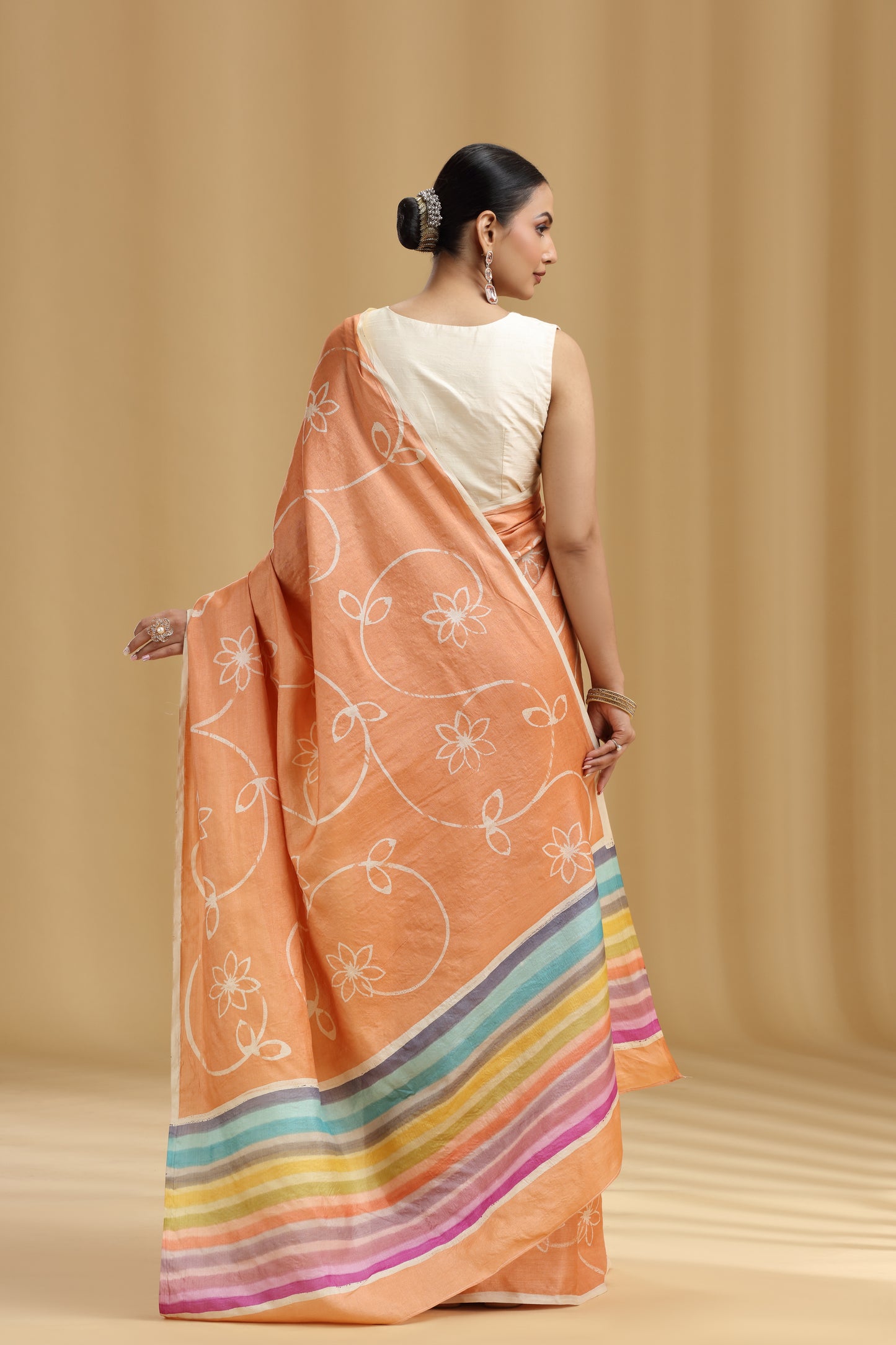Woman wearing a peach saree with colorful stripes on a beige background