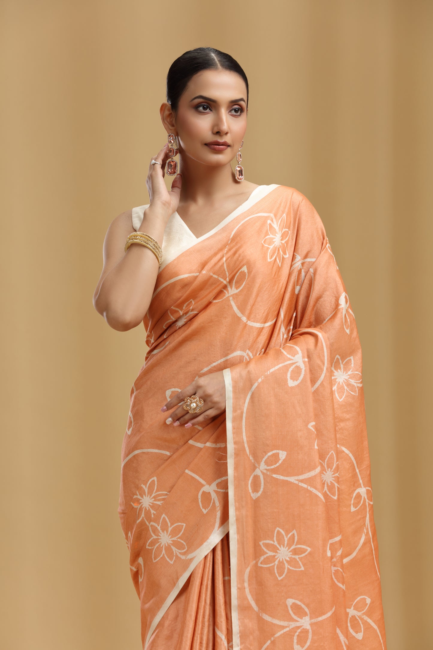 Woman wearing an peach saree with white floral patterns on a beige background