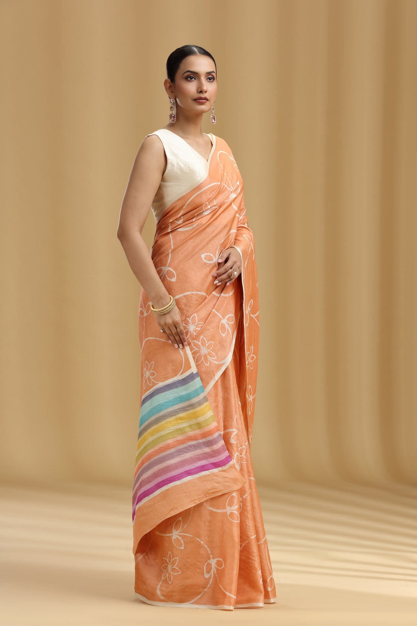 Woman wearing an peach saree with a rainbow design on a beige background