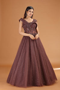 Woman wearing a brown net gown with intricate detailing on an orange background