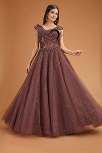 Woman wearing a brown evening net gown with intricate detailing on a brown background