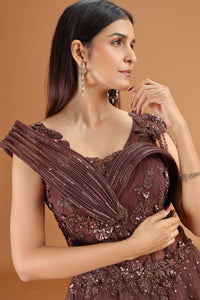 Woman wearing an elegant brown dress with intricate detailing on a beige background