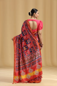 Woman wearing a vibrant red saree with intricate patterns on a beige background
