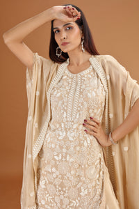 Woman wearing a beige embroidered salwar suit with a matching dupatta against a brown background