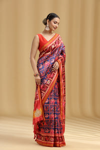 Woman wearing a traditional patola silk saree with a red and blue pattern on a beige background