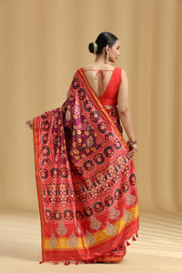 Woman wearing a red purple silk saree with intricate patterns on a beige background