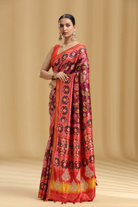 Woman wearing a red and orange purple patola silk saree with intricate patterns on a beige background