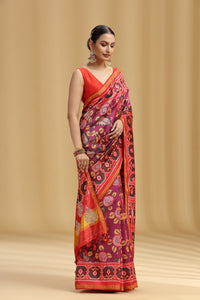 Woman wearing a vibrant patola silk saree with a pattern against a beige background