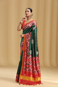Woman wearing a green and red patola silk saree with floral patterns on a beige background