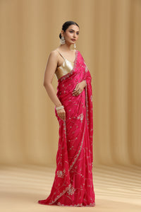 Woman wearing a pink designer saree with gold blouse against a beige background