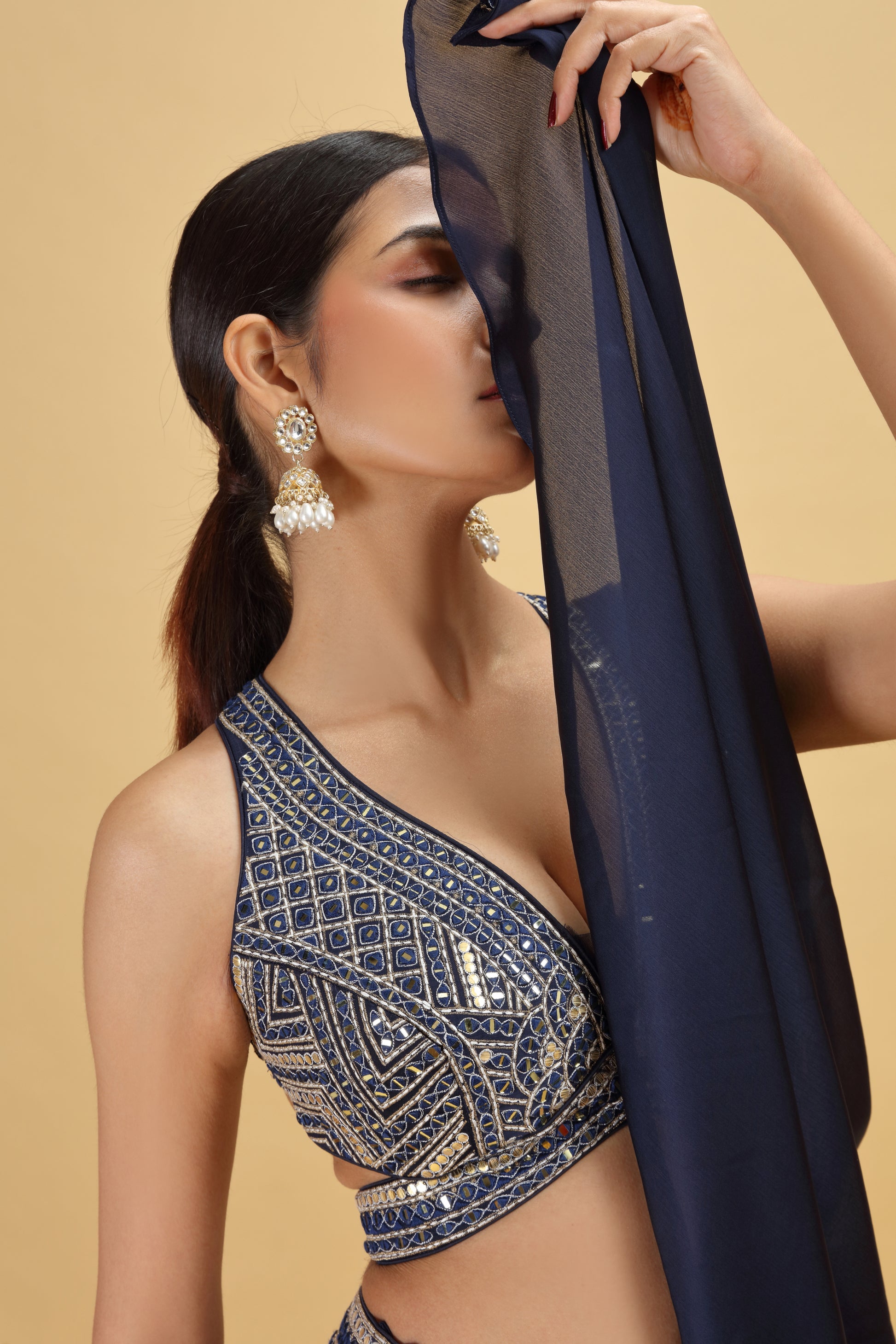 Woman holding a navy blue fabric against a beige background wearing a matching blouse with mirror work