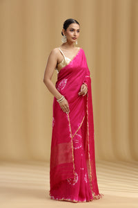 Woman wearing a bright pink saree with a gold border on a beige background