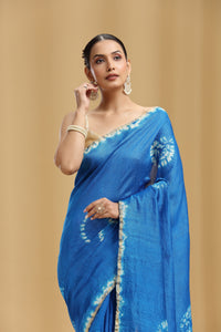 Woman wearing a blue silk saree with white patterns on a beige background