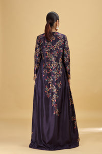 Woman wearing a long, dark purple suit with floral embroidery on a beige background
