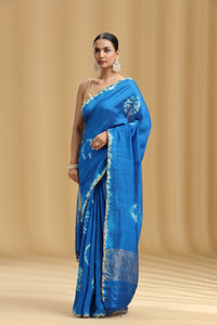 Woman wearing a blue saree with white patterns on a beige background