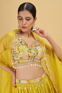 Woman wearing a bright yellow traditional outfit with colorful embellishments on a beige background