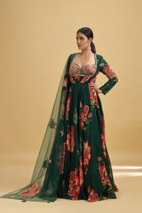 Woman wearing a green floral dress with a sheer dupatta against a beige background